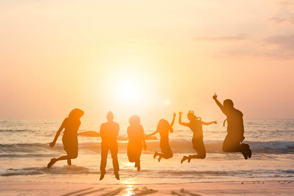 A group of friends jump in the air near the sea at sunset.