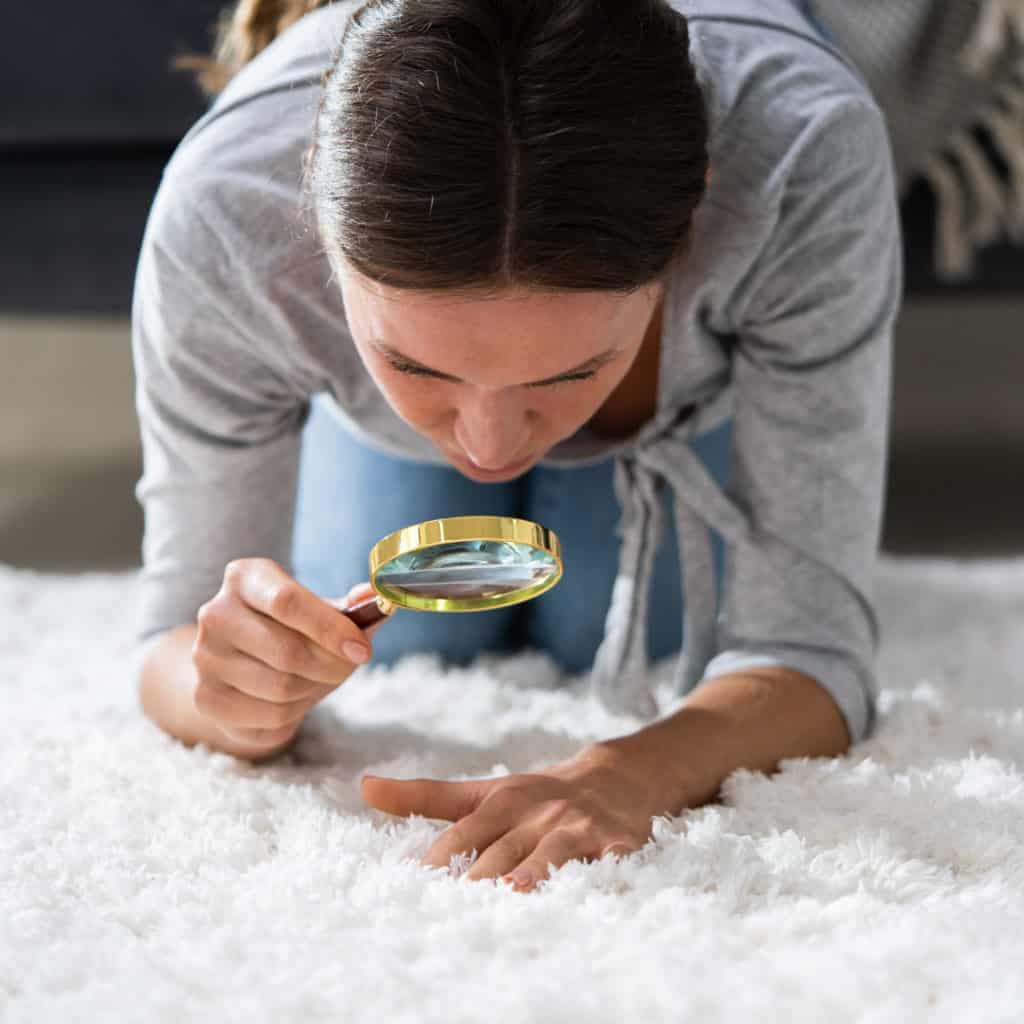 Woman looking at carpet with a magnifying glass
